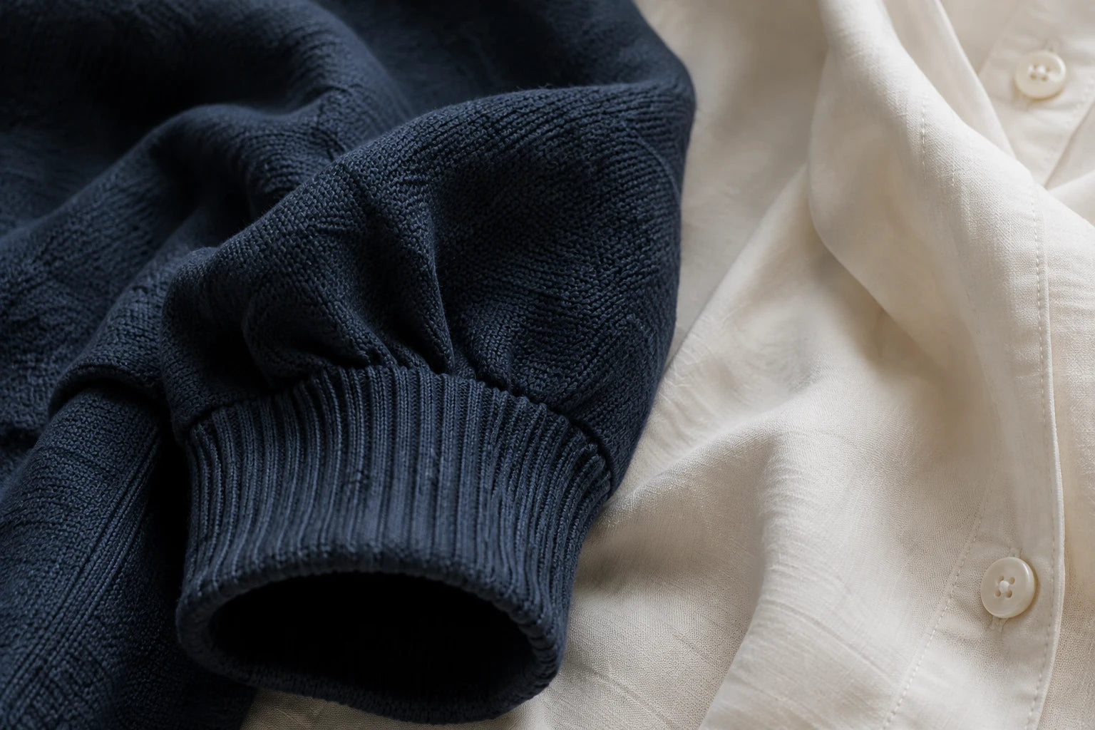 Navy knitted cuff beside an ivory cotton shirt.